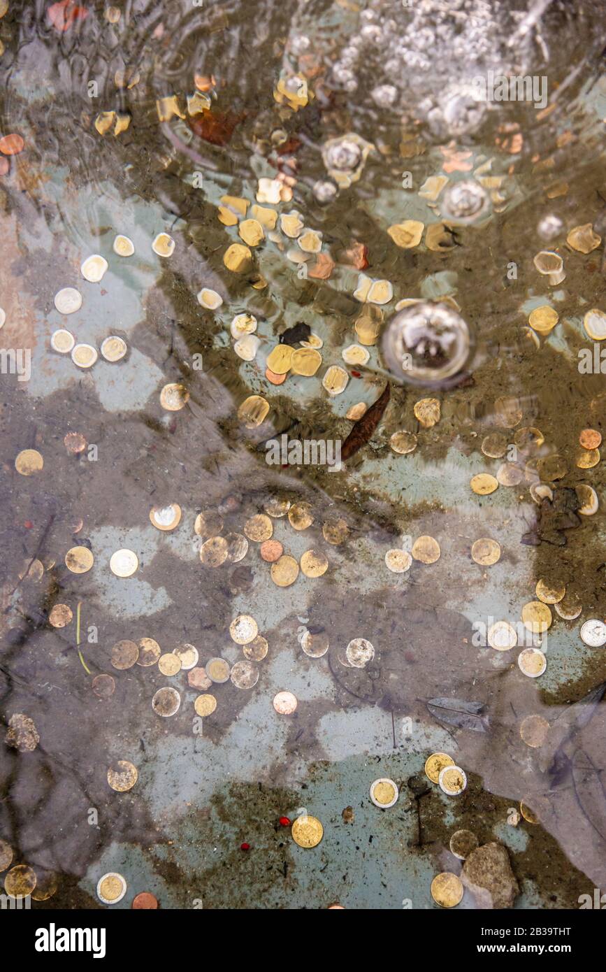 Münzen am Boden eines Brunnens, die durch die Vergrößerung des Wassers gesehen werden, das sie verformt, zeigen Blasen an der Wasseroberfläche. Konzentrieren Sie sich auf die Münze Stockfoto