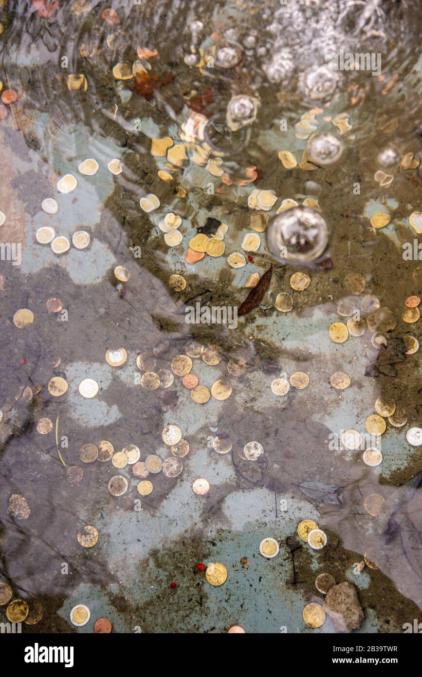 Münzen am Boden eines Brunnens, die durch die Vergrößerung des Wassers gesehen werden, das sie verformt, zeigen Blasen an der Wasseroberfläche. Konzentrieren Sie sich auf die Münze Stockfoto