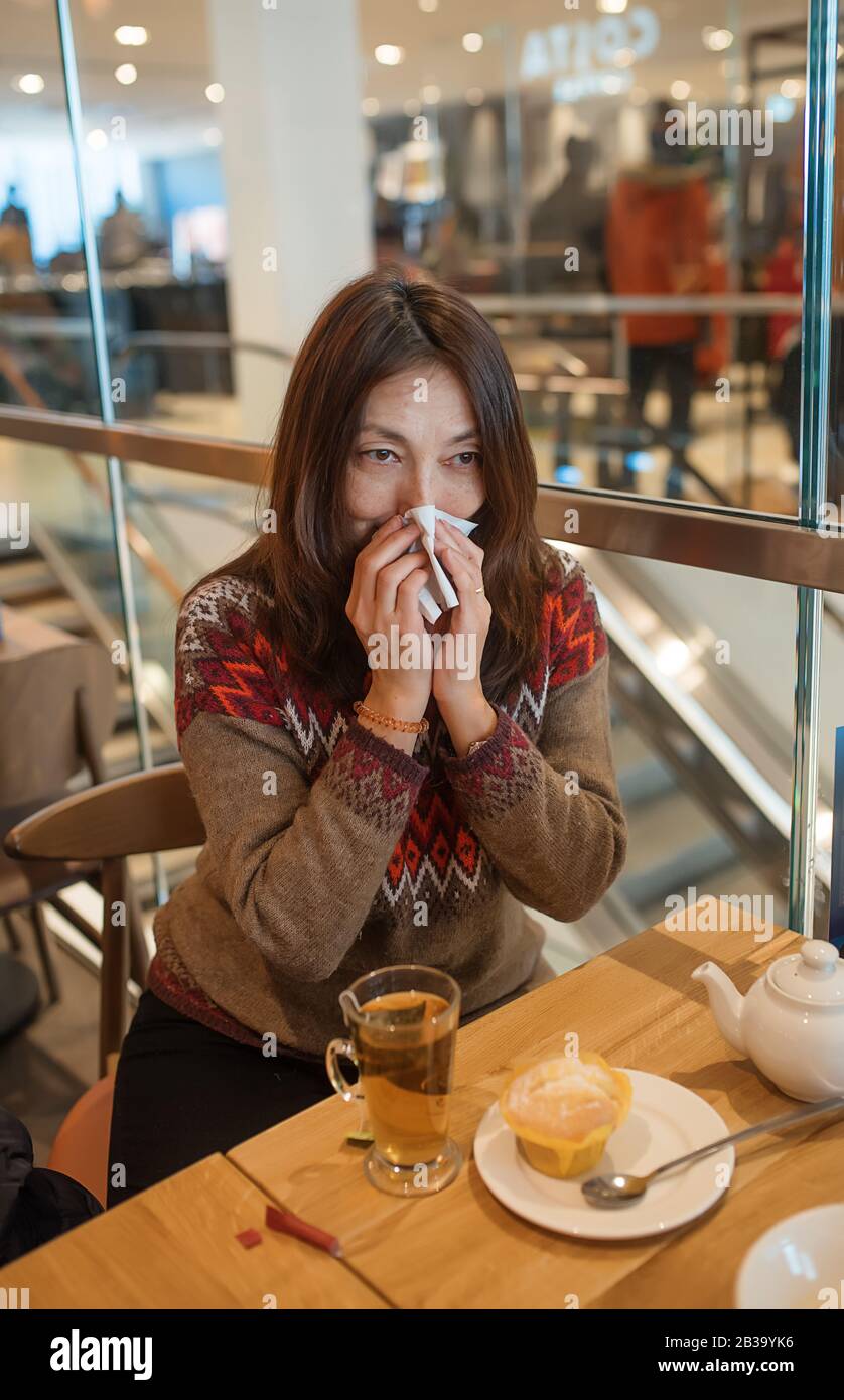 Nette asiatische junge Frau, die nach dem Einkaufen in einem Café die Nase wischt und eine Tasse Tee hat Stockfoto