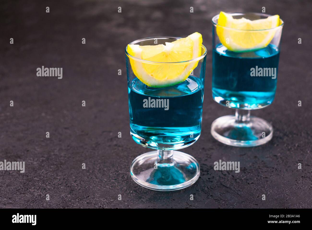 Blauer alkoholischer Cocktail mit einer Zitronenscheibe auf schwarzem Hintergrund. Kopierbereich. Stockfoto