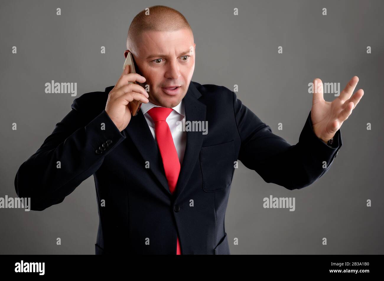 Der in schwarzem Anzug gekleidete Geschäftsmann, der am Telefon spricht, beginnt nervös mit der Hand herumzu gestikulieren Stockfoto
