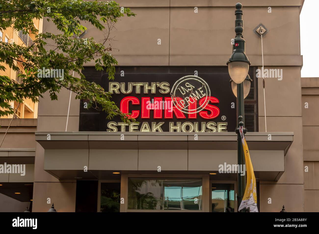 Charlotte, NC/USA - 26. Mai 2019: Mittlere Nahaufnahme der Steakhausfassade "Ruth's Chris" mit einer Marke über dem Eingang mit Lampenpfosten und Baumzweigen. Stockfoto