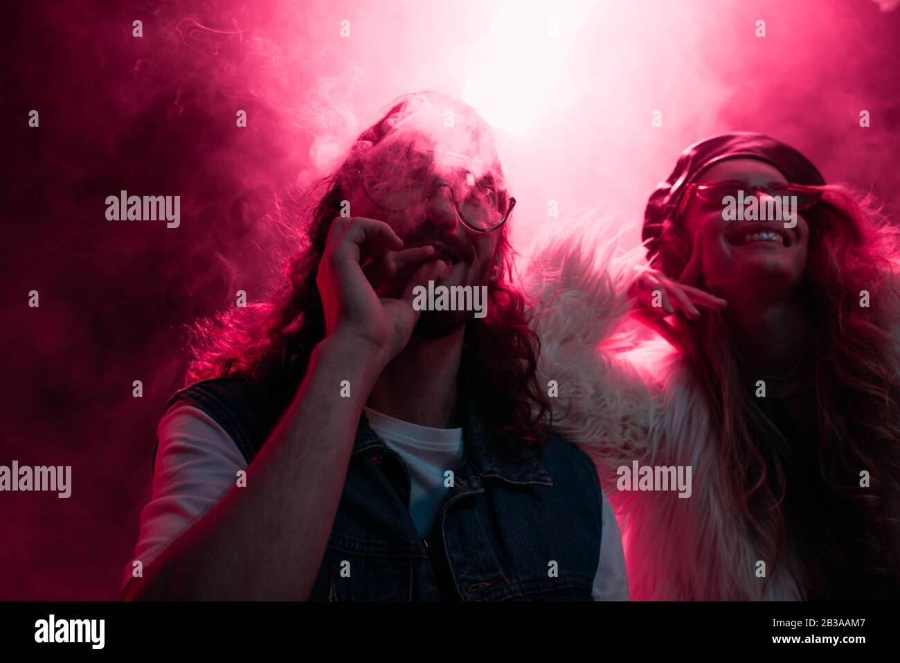 Mann raucht Marihuana-Joint in der Nähe eines lächelnden Mädchens im Nachtclub Stockfoto