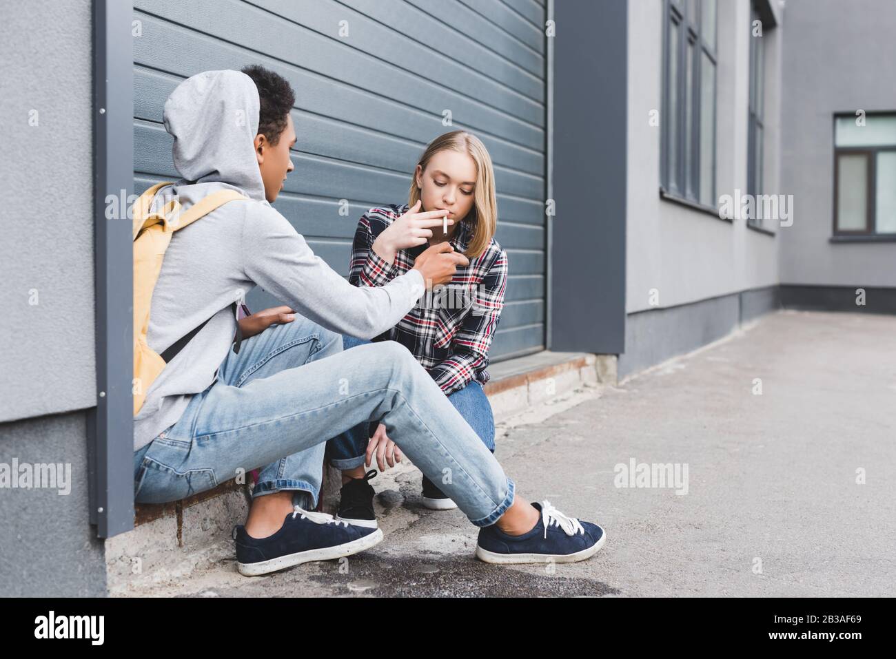 afroamerikanischer Junge, der eine Zigarette blonder und hübscher Teenager zündet Stockfoto