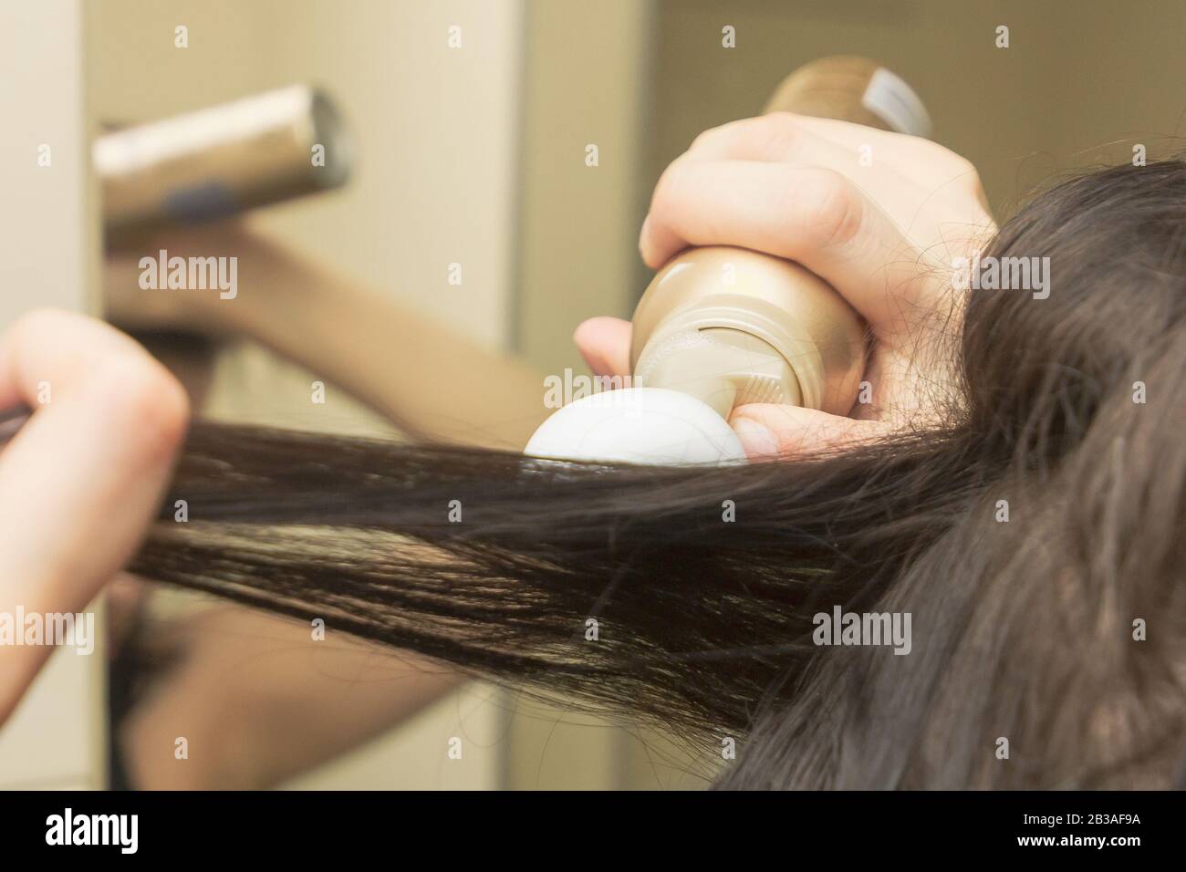 Junge Frauen stylen ihr Haar mit einem Schaum oder einer Mousse. Styling Mousse auf dem braunen langen geraden Haar. Stockfoto