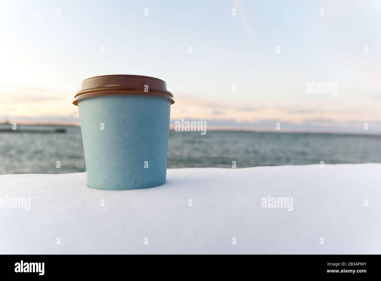 Nehmen Sie Kaffee mit Meeresgrund im Winter. Winterschnee nehmen Sie den Sonnenuntergang über der Kaffeetasse auf dem Meer weg Stockfoto