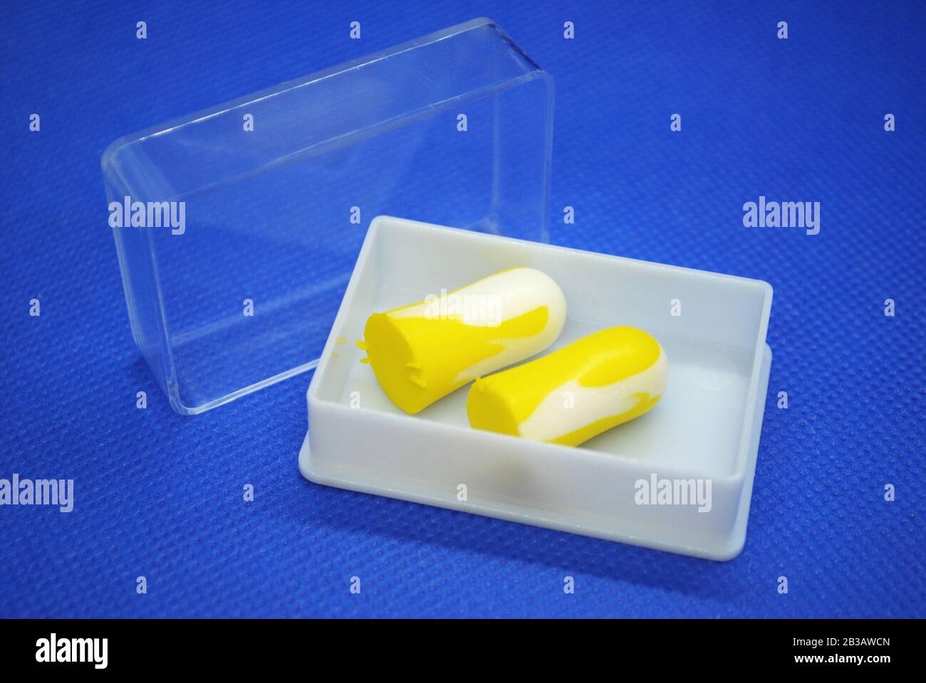 Isoliertes Paar bunt weißer und gelber Ohrenstöpsel in einer weißen Kunststoffbox mit transparenter Abdeckung auf blauem Hintergrund Stockfoto
