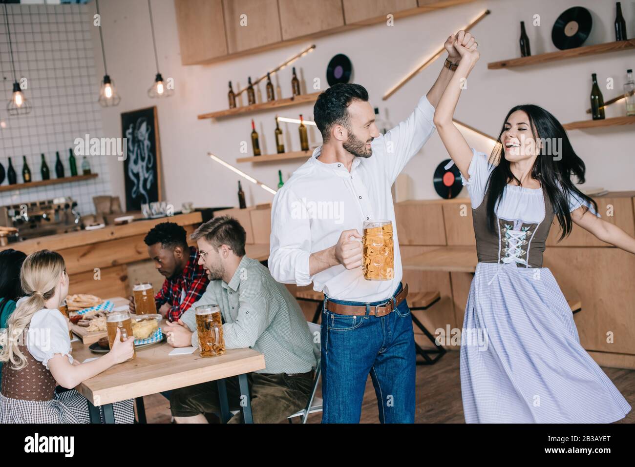 Gutaussehender junger Mann, der im traditionellen deutschen Kostüm mit schöner Frau ein Glas Bier tanzt Stockfoto