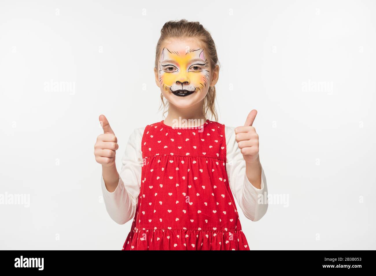 Glückliches Kind mit Tiger-Schnauze-Malerei auf dem Gesicht, das die Daumen nach oben isoliert auf Weiß zeigt Stockfoto