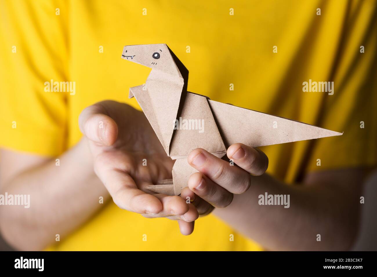 Mädchen, die Origami-Dinosaurier in den Händen halten, auf einem gelben Hintergrund. Interessantes Hobby Stockfoto