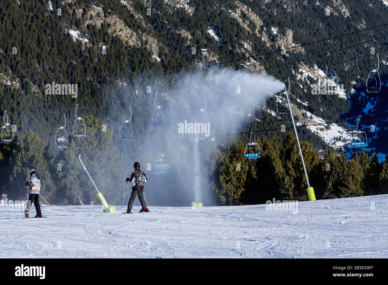 Schneekanonen, die auf der Skipiste Neuschnee bläsen. Skifahrer auf Pisten mit Sesselliften und Pyrenäenbergen im Hintergrund. El Tarter in Grandvalira, Andorra Stockfoto