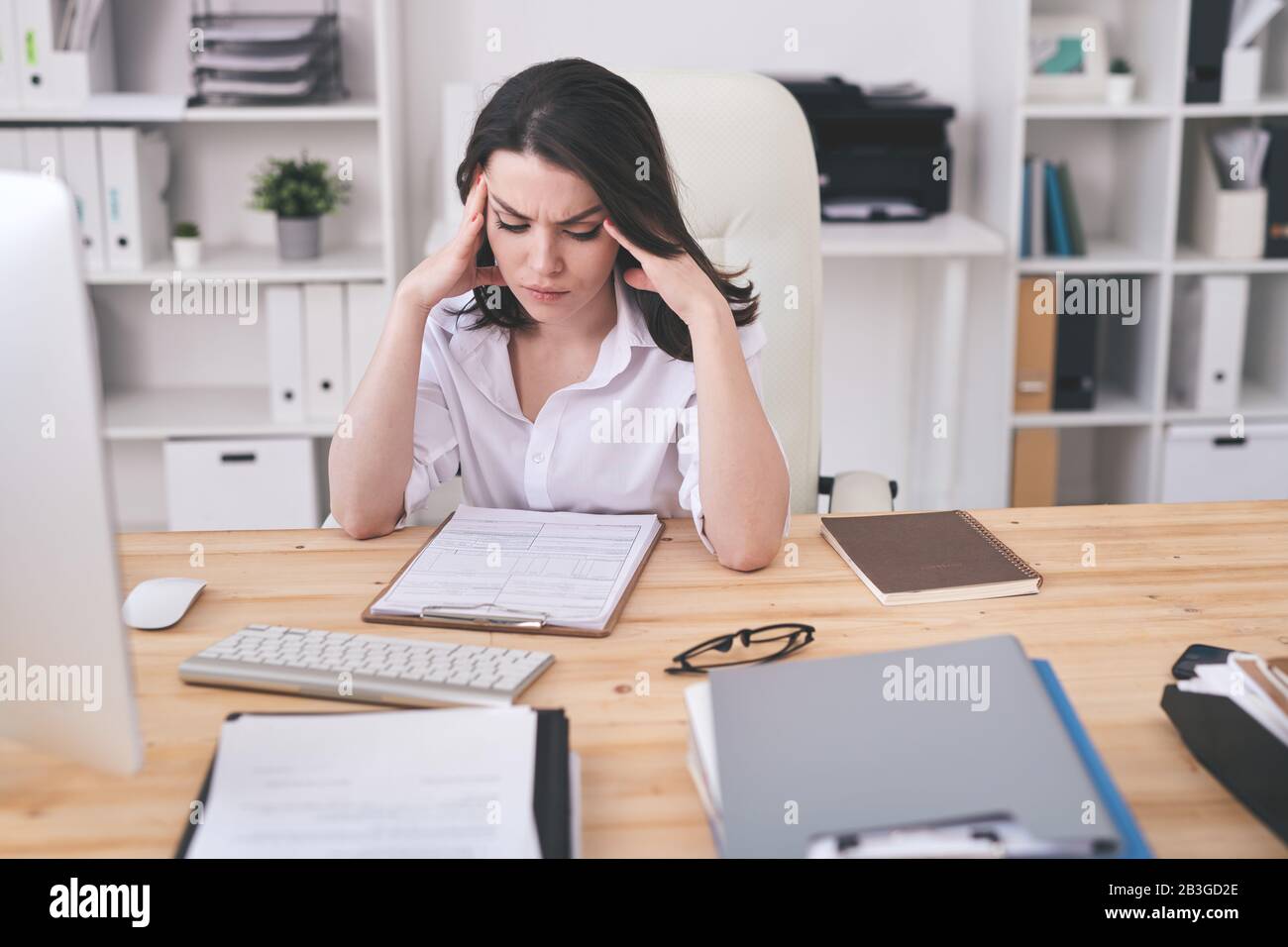 Verwirrte junge Geschäftsfrau, die im modernen Büro am Schreibtisch sitzt und Vertragsinhalte analysiert Stockfoto