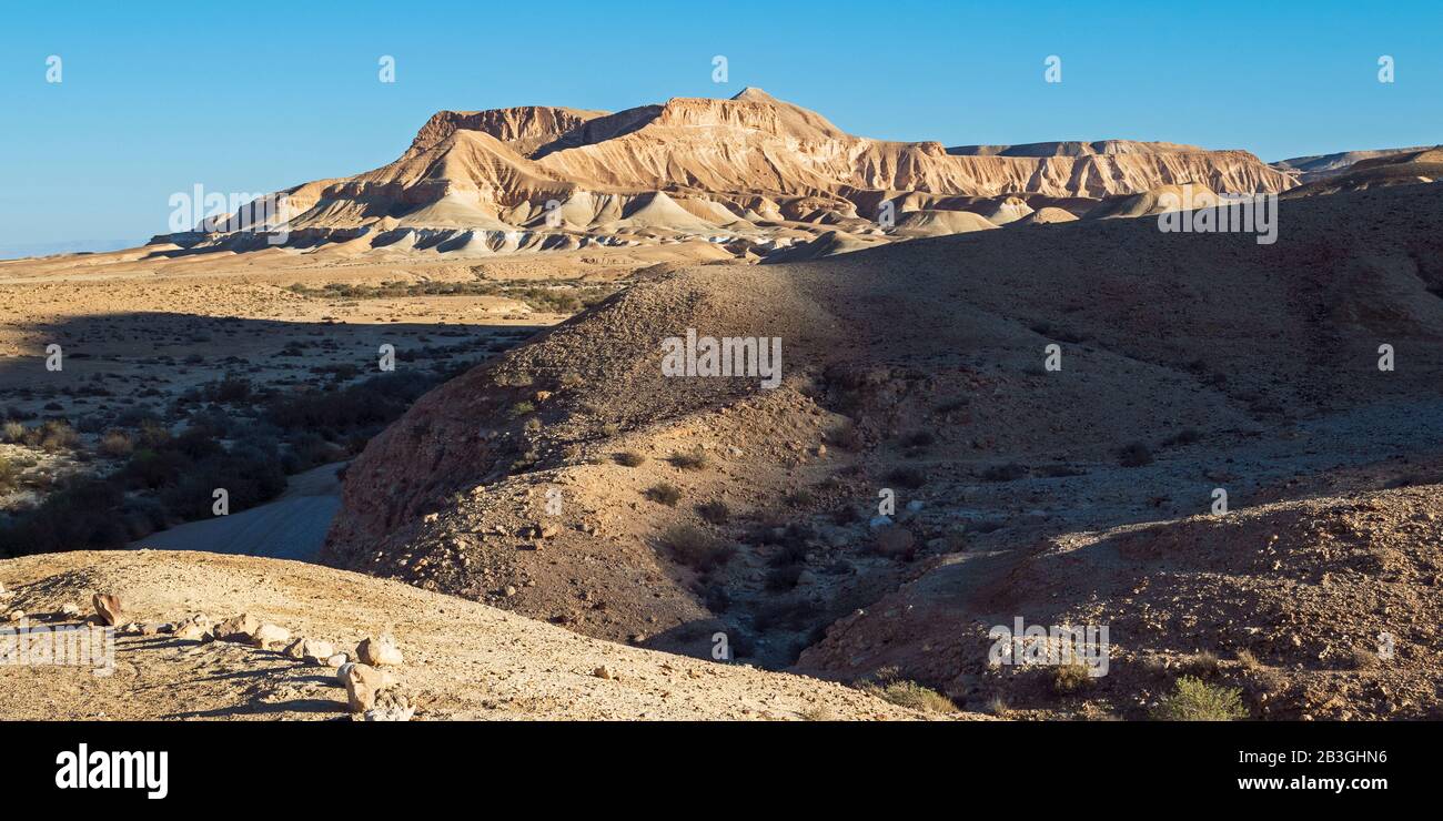 Schatten der untergehenden Wintersonne umrahmen Akev und Berggipfel im Tal von Zin in israel mit einem klaren blauen Himmel im Hintergrund Stockfoto