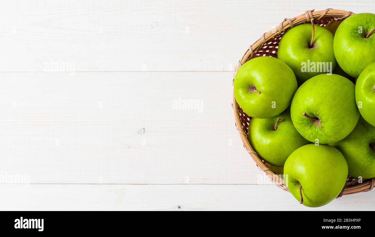 Äpfel-Ernte-Konzept. Bamboo Basket mit grünen Äpfeln auf weißem Holzhintergrund mit Platz für Text oder Design. Draufsicht oder flache Lage. Banner Stockfoto