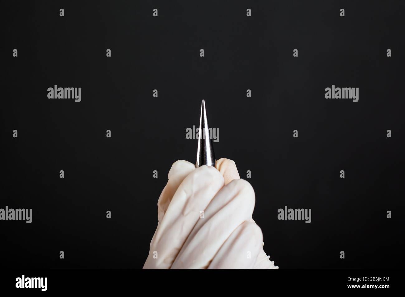 Hand in einen weißen Einweg-Handschuh-Ohr-Expander zum Durchstechen von Tunneln auf dunklem Hintergrund in Nahaufnahme. Stockfoto