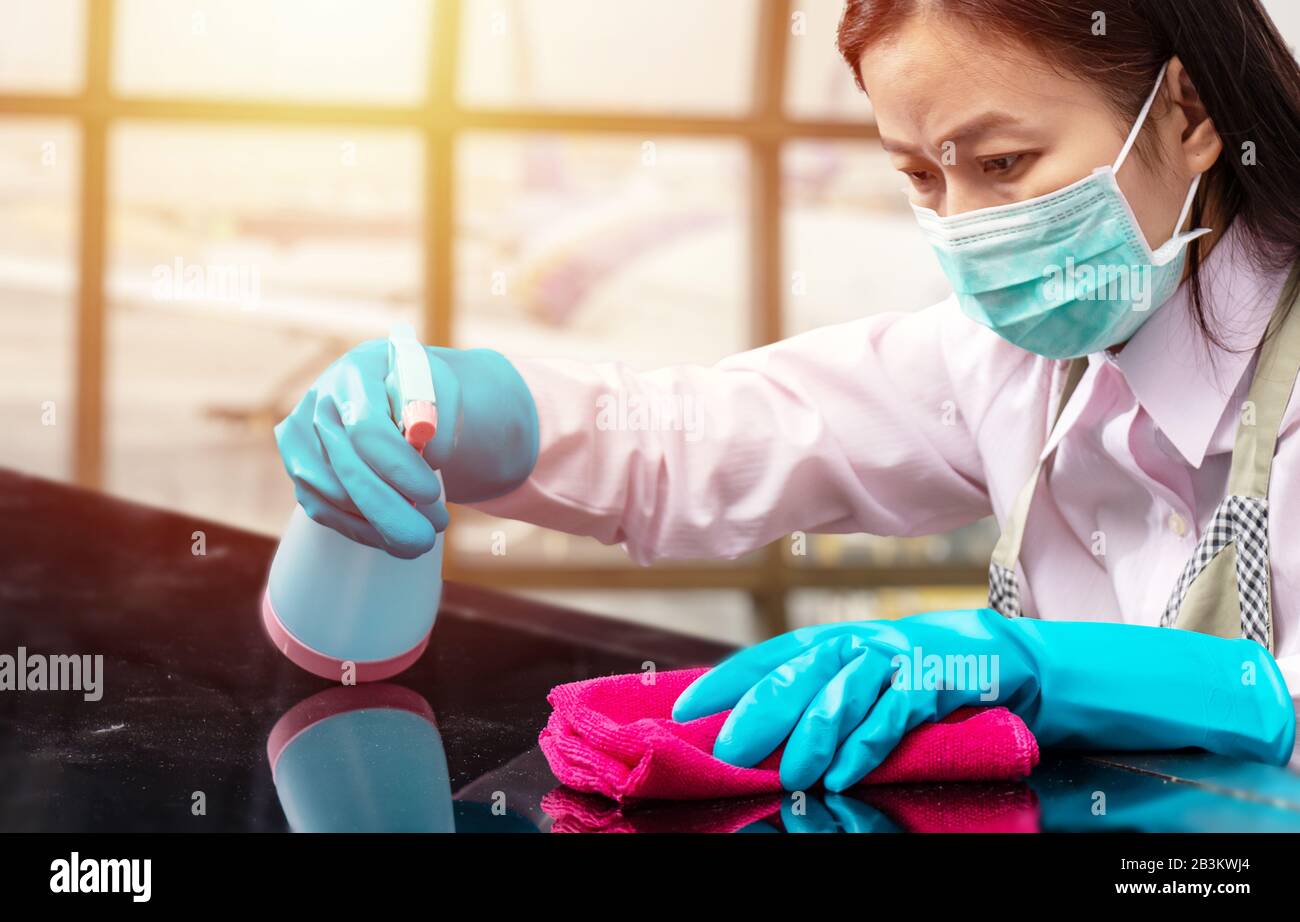 Flughafenmitarbeiter tragen eine hygienische Gesichtsmaske und einen blauen Gummihandschuh, der das pinke Mikrofaser-Reinigungstuch und die Sprühflasche mit der Sterilisationslösung hält Stockfoto