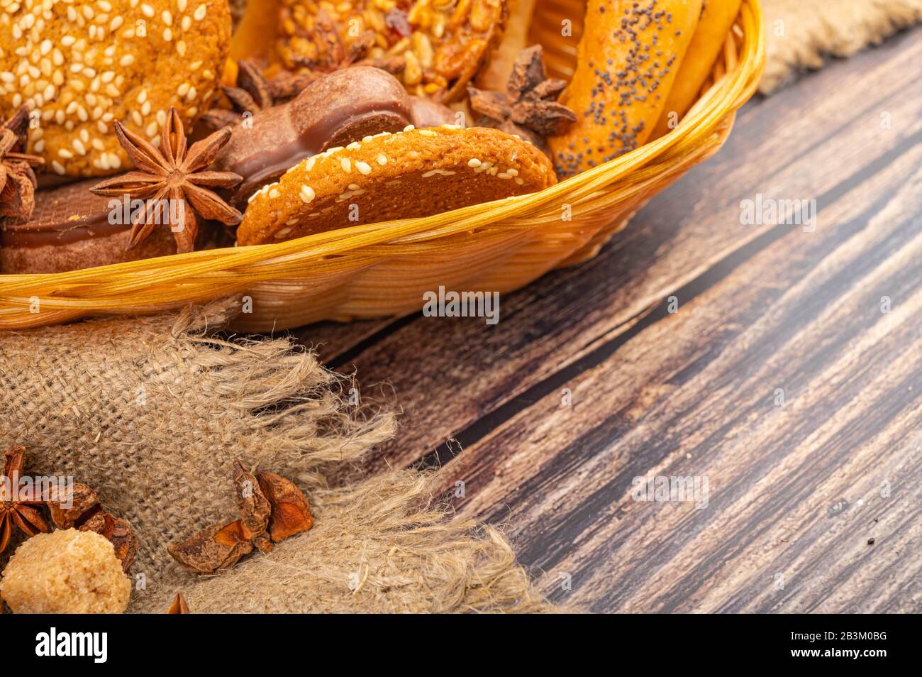 Plätzchen, Schokoladenkuchen, Bagels und Sternanis in einem Korbkorb auf Holzgrund. Nahaufnahme Stockfoto