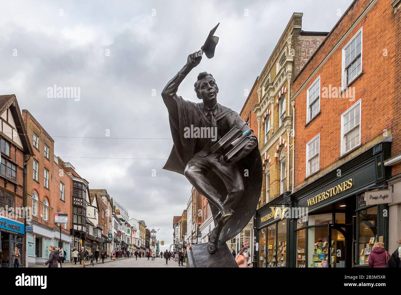 Die Surrey Scholar-Skulptur, die an der Guildford High Street steht. Eine dynamische Skulptur eines Absolventen in Mütze und Gown, die einen Hauch von Büchern überhäuft. Stockfoto