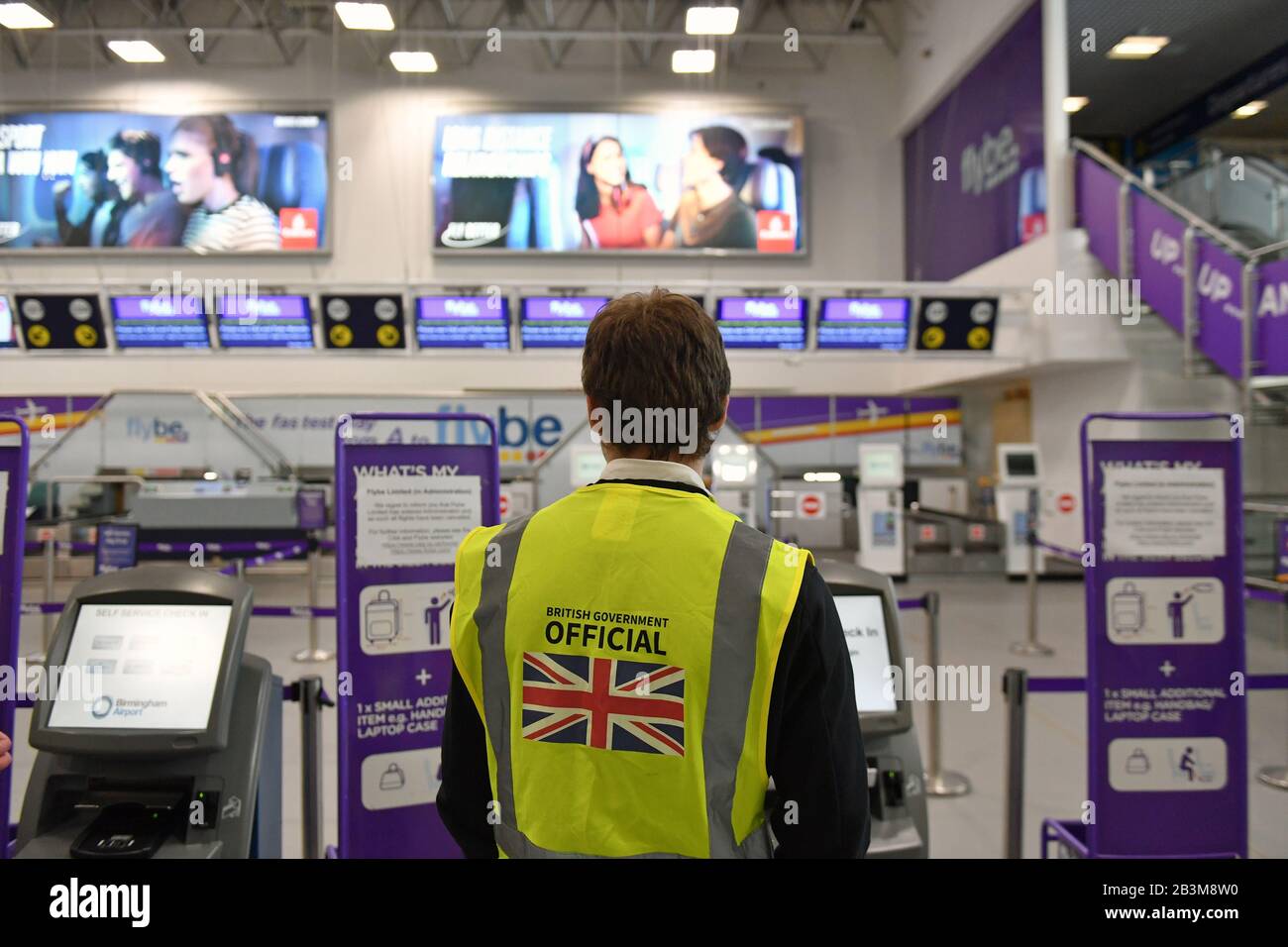 Ein Beamter der britischen Regierung steht an den leeren Flybe Check-in-Schaltern am internationalen Flughafen Birmingham, da Flybe, Europas größte regionale Fluggesellschaft, in die Verwaltung eingebrochen ist. Stockfoto