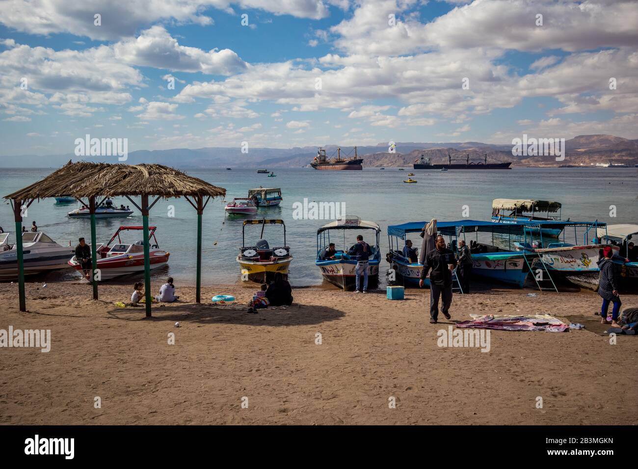 Aqaba, JORDANIEN - 31. JANUAR 2020: Lokale Menschen und Touristen genießen Freitag am sonnigen Stadtstrand mit Glasbodenbooten Urlaub. Winter puffige Wolken Morgenhimmel. Rotseegulf, Haschemitisches Königreich Jordanien Stockfoto