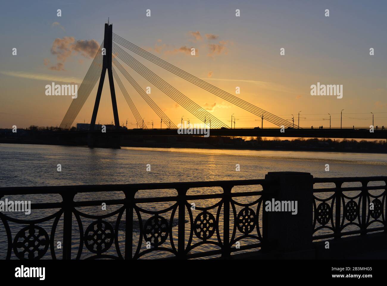 Die Silhouette der Kabelstreusbrücke liegt mit kleinen Wolken gegen den schönen Himmel. Dies ist ein Sonnenuntergang in der europäischen Stadt Riga. Stockfoto