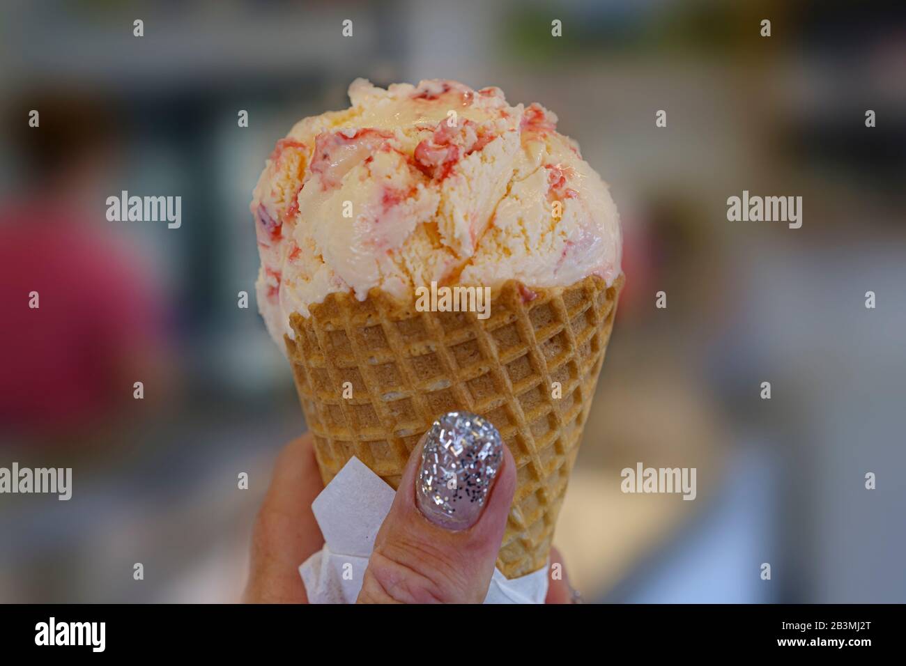 Eine Frauenhand hält ein Gelb mit rotem Eis. Stockfoto