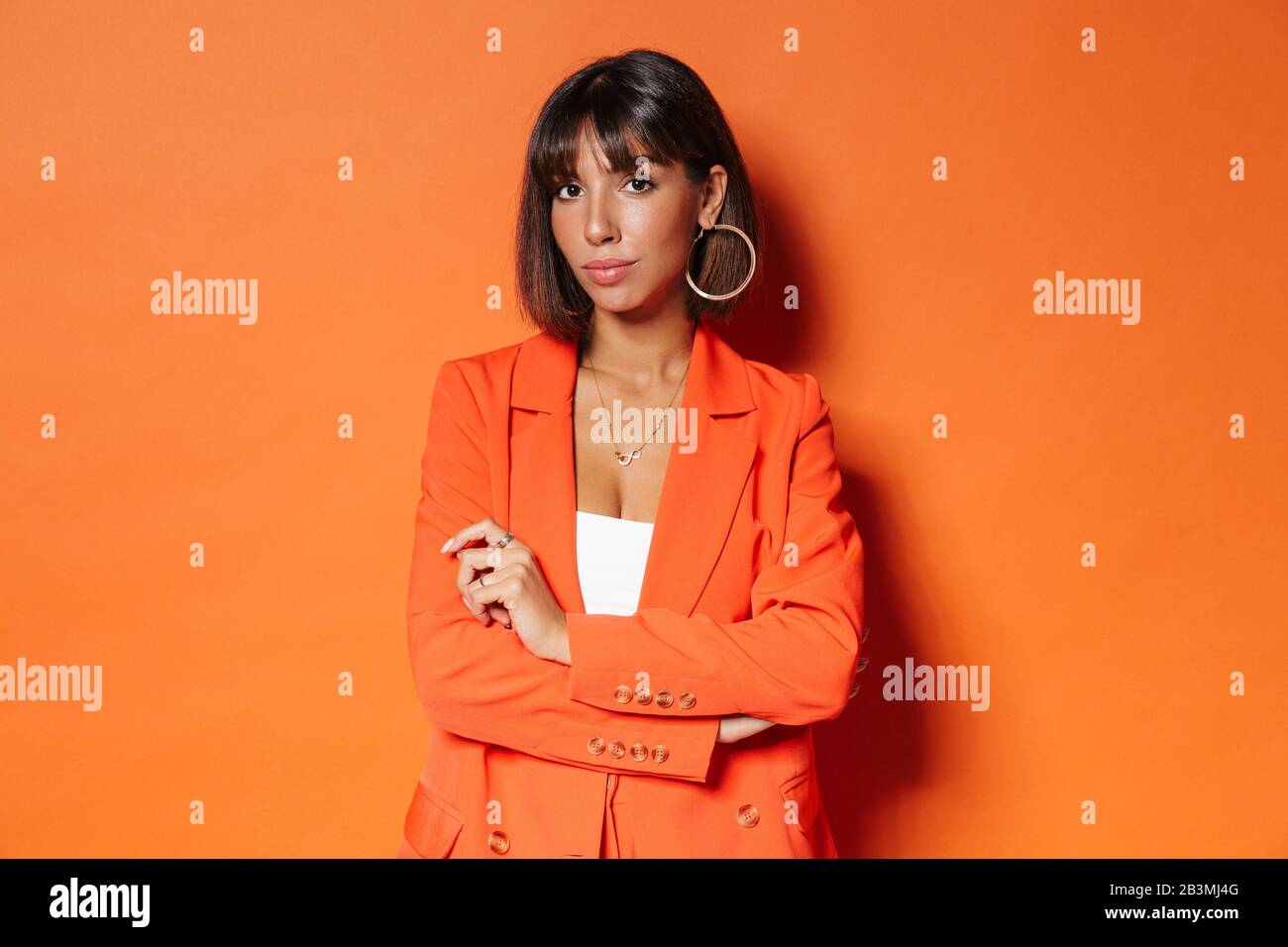 Porträt einer schönen jungen braunen kurzhaarigen Frau, die Anzug trägt, der über orangefarbenem Hintergrund steht und posiert Stockfoto