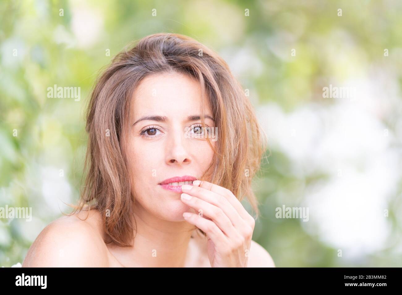 Porträt einer natürlichen Frau in ihren dreißiger Jahren ohne Make-up in einer Natureinstellung mit grünen Blättern eines Baumes im Hintergrund. Stockfoto