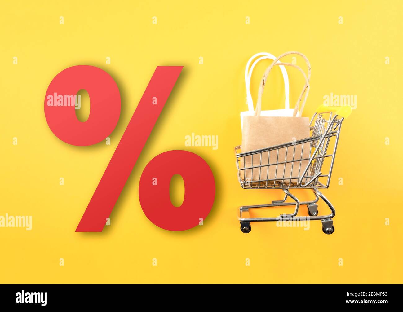 Einkaufswagen mit Einkaufstaschen und großem roten Prozentzeichen vor gelbem Hintergrund, Einzelhandelsverkauf und Rabattkonzept Stockfoto