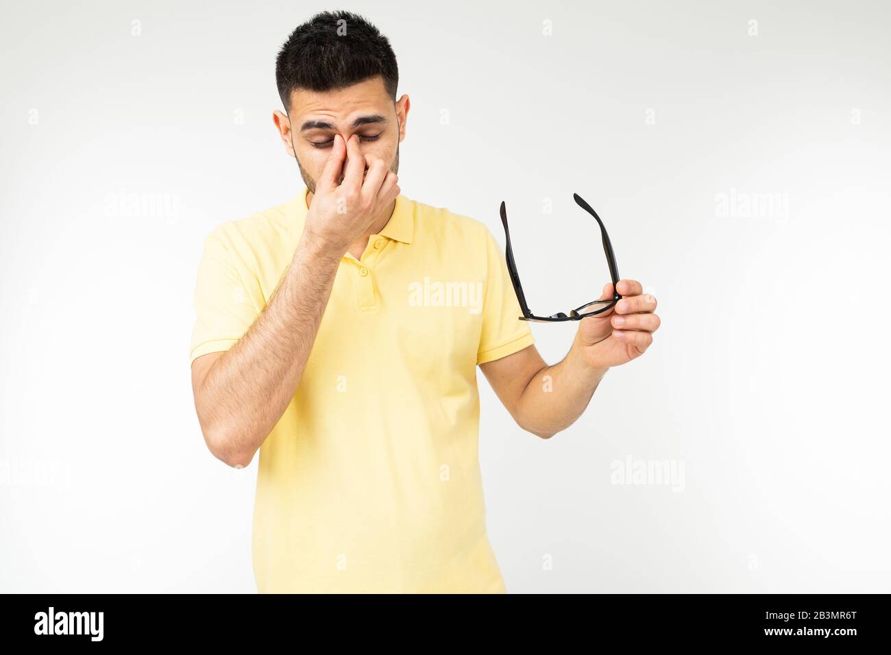 Guy fühlt Schmerzen in seinen Augen, indem er seine Brille entfernt, um auf einem weißen Hintergrund zu sehen Stockfoto