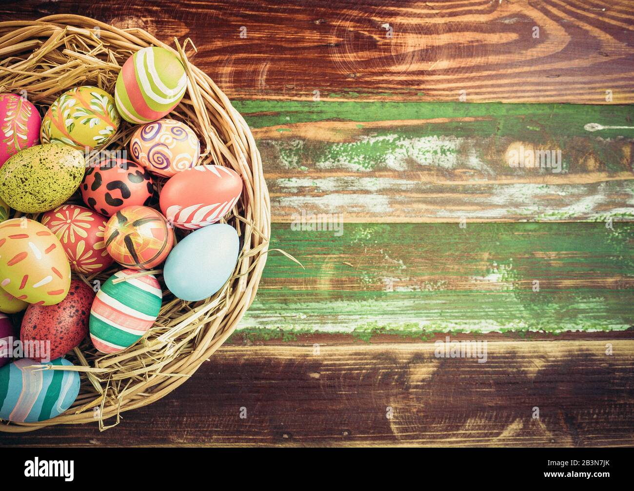 Ostereier in verschiedenen Mustern und Farben in einem Vogelnest auf einem Holzboden, der im Retro-Stil dekoriert ist. Stockfoto