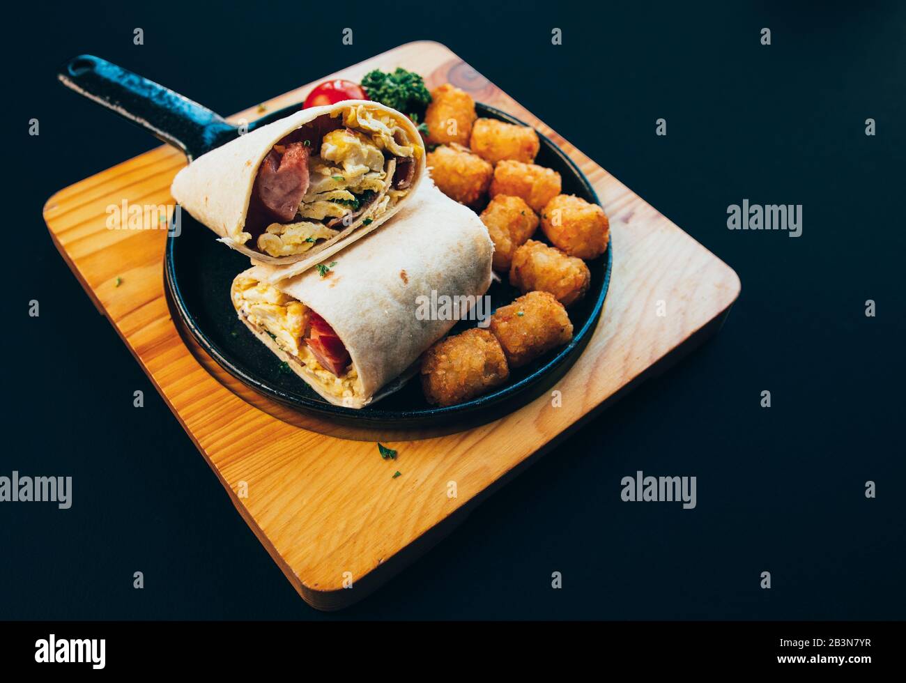 Brunch Burrito im amerikanischen Stil mit Rührei, Würstchen, Hashbraun und Tomaten. Stockfoto