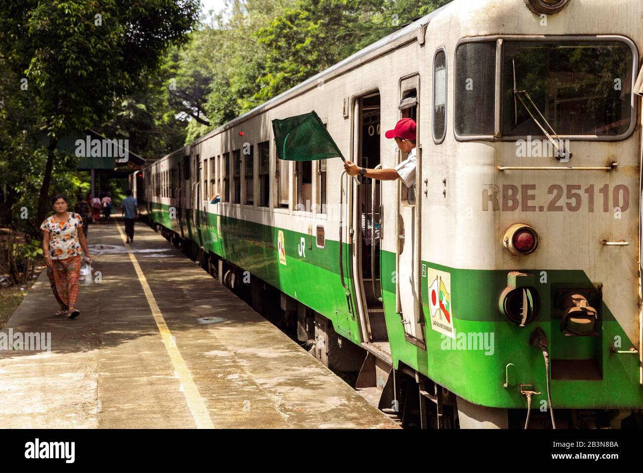 Ein Personenzug am Bahnhof Lanmadaw mit Zugleiter schwenkt eine grüne Flagge und ein Passagier auf dem Bahnsteig, Yangon (Rangun), Myanmar (Birma), Asi Stockfoto