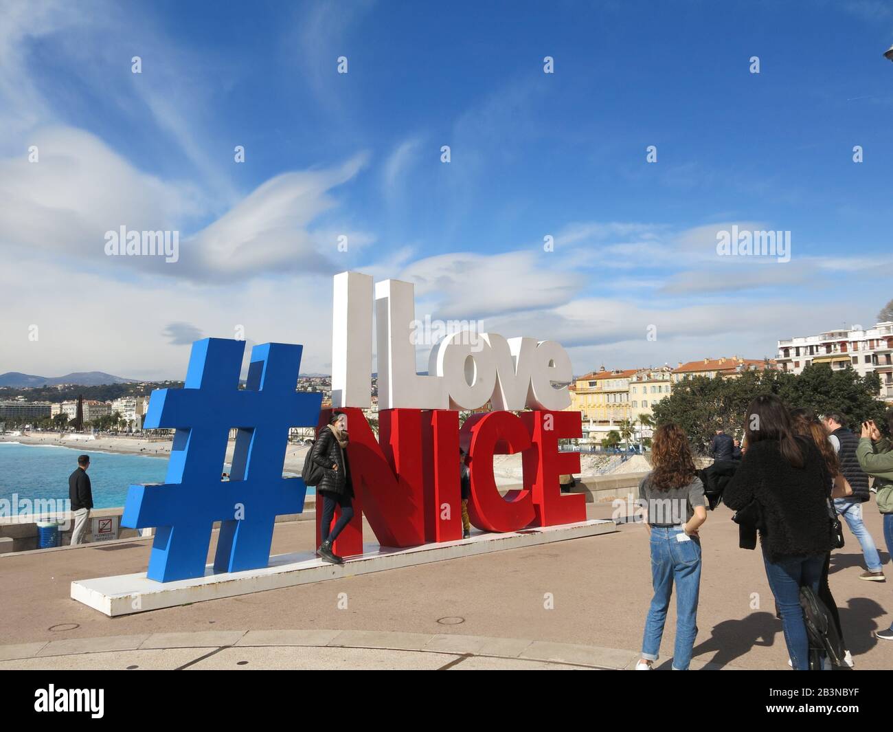 Ein beliebter Ort für Fotos, Touristen stehen an einem sonnigen Frühlingstag an einem Ende der Promenade des Anglais unter dem großen Slogan von '# I Love NICE'. Stockfoto