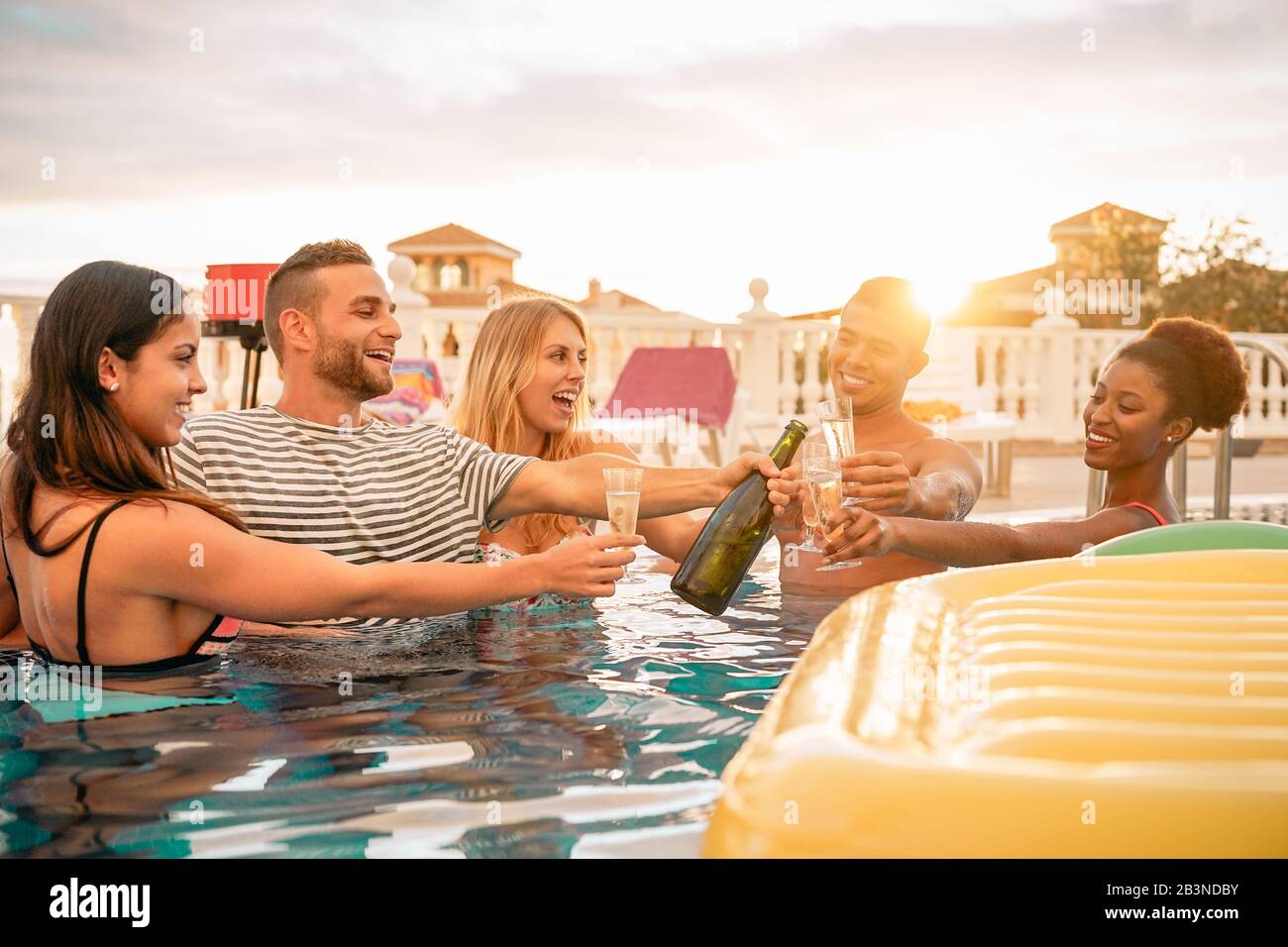 Fröhliche Freunde, die Champagner auf der Poolparty toben - Junge Leute, die Spaß haben, Sekt im luxuriösen tropischen Resort bei Sonnenuntergang zu trinken Stockfoto