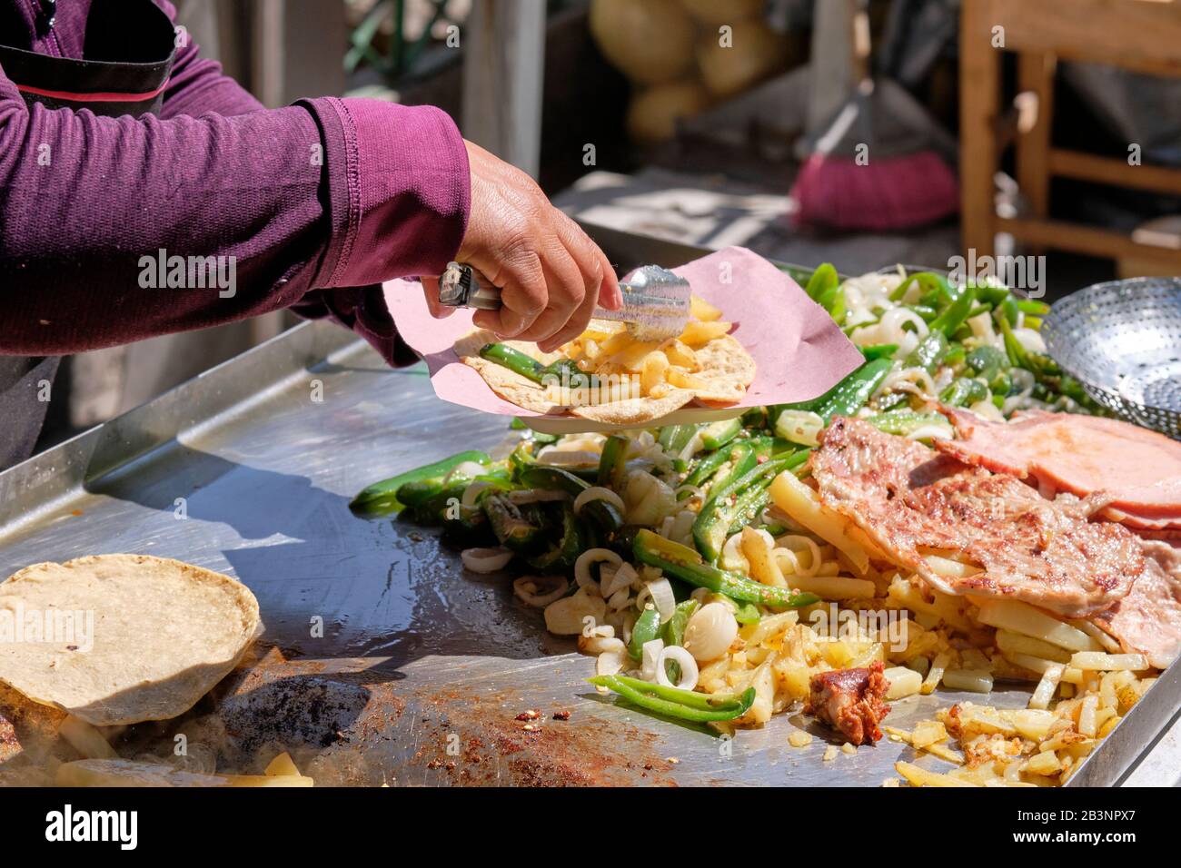 Die Hand der Frau, die einen gemischten Grillteller auf einem Taco im mexikanischen Outdoor-Speisewagen serviert, wo sie verschiedene Fleischsorten und Gemüse in einem Karneval braten Stockfoto