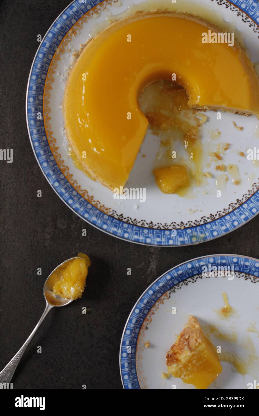 Große brasilianische Kokosnuss- und Eigelb-Pudding-Kuchen, genannt Quinim, auf einem weißen und blauen Teller mit einem Löffel Stockfoto