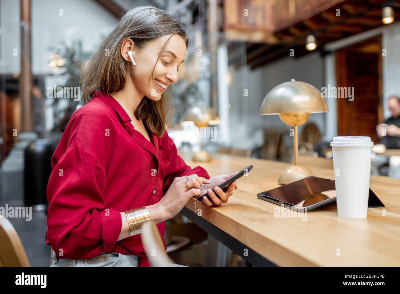 Portrait einer jungen, stilvollen Frau, in Rot gekleidet, mit Handy am Tisch im schönen Café, im feigen Raum oder im Lesesaal der Bibliothek Stockfoto