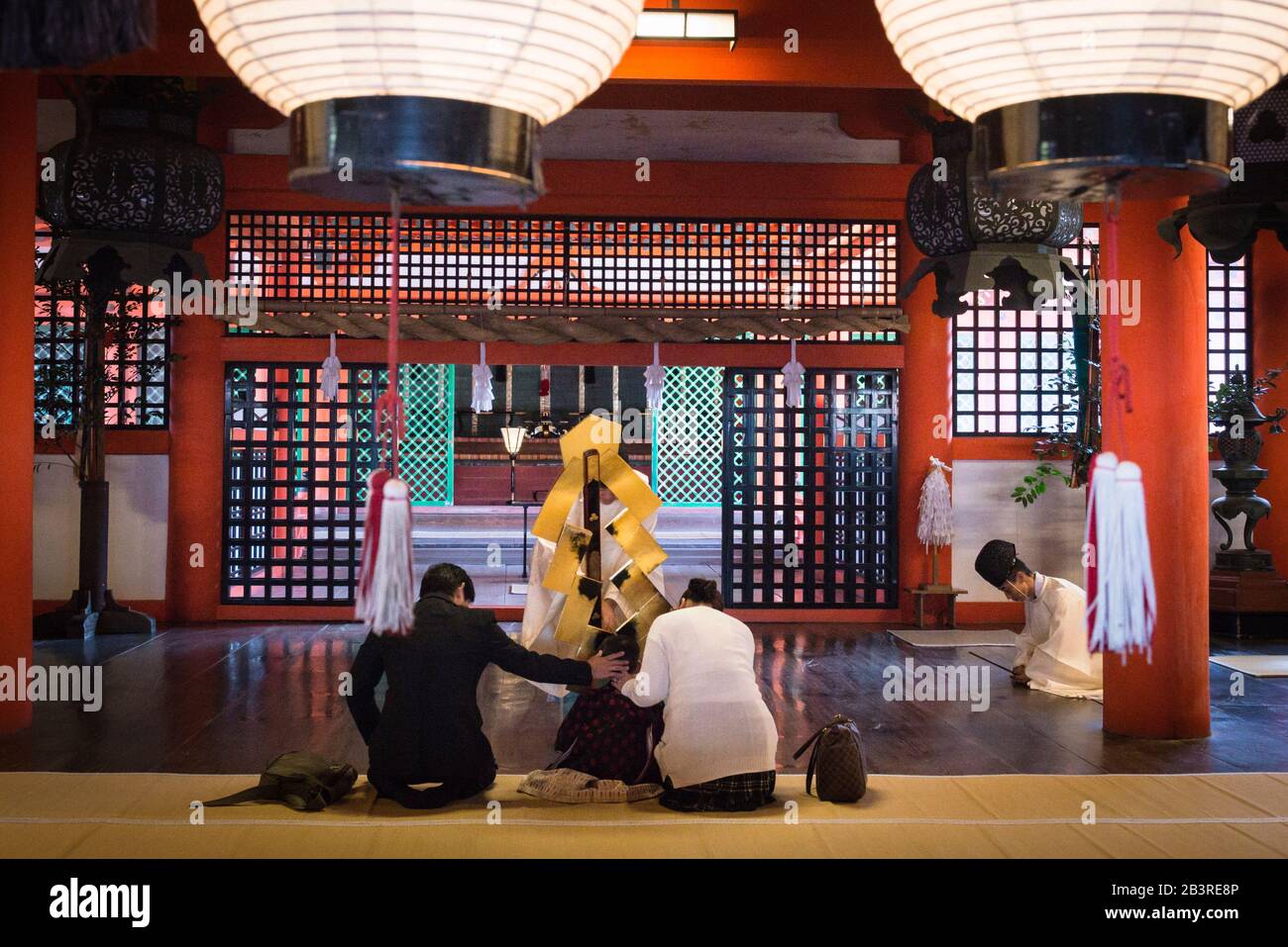 Der Shinto Priester segnet scheinbar den jungen Jungen, der zwischen zwei Erwachsenen auf öffentliche Sicht sitzt, im Marodo-Schrein im Itsukushima-Schrein, Miyajima Stockfoto