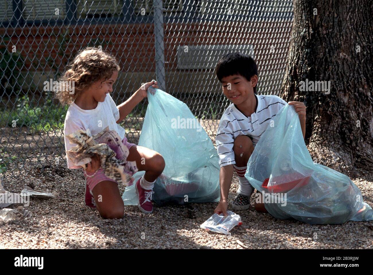 Austin Texas USA: Acht- und neunjährige Jungen und Mädchen holen auf dem Schulgelände Müll ab. ©Bob Daemmrich Stockfoto