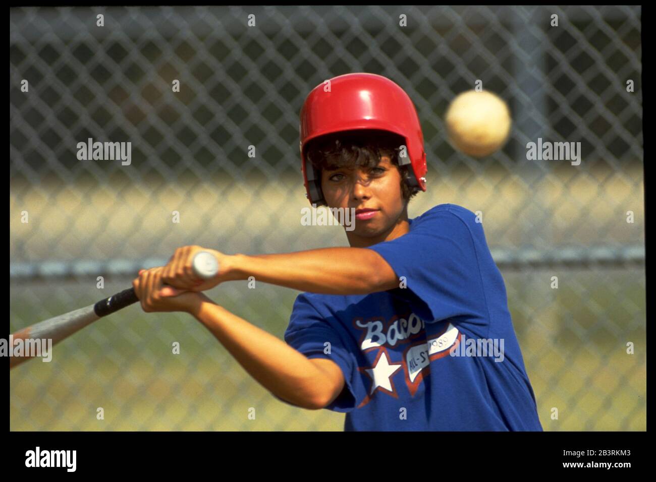 Austin Texas USA, 1990: Das hispanische Teenager-Mädchen mit Schlaghelm hält ihr Auge auf den Softball, während sie sich darauf vorbereitet, ihre Fledermaus zu schwingen. HERR ©Bob Daemmrich Stockfoto