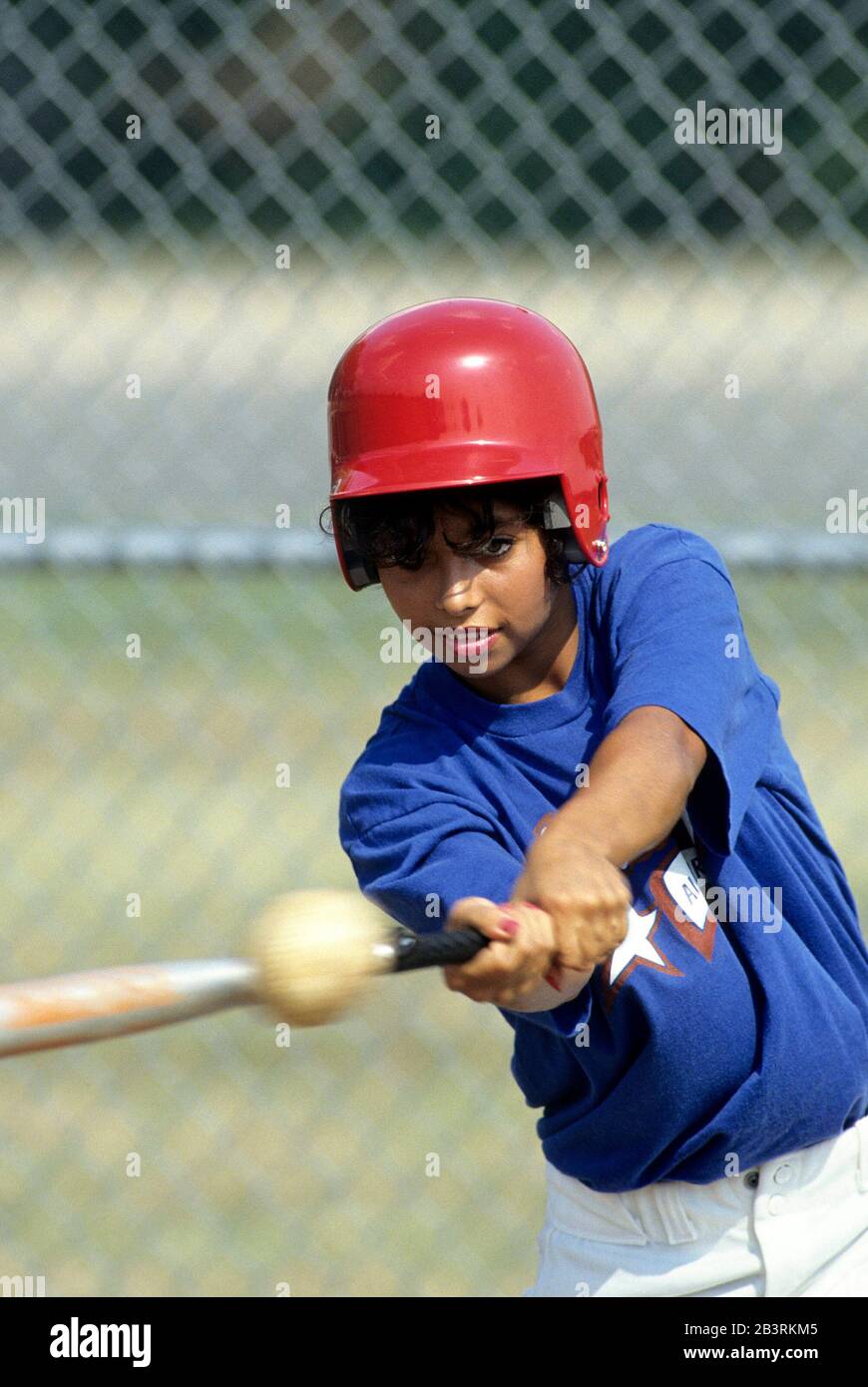 Austin Texas USA, 1990: Das hispanische Teenager-Mädchen mit Schlaghelm hält ihr Auge auf den Softball, während sie sich darauf vorbereitet, ihre Fledermaus zu schwingen. HERR ©Bob Daemmrich Stockfoto