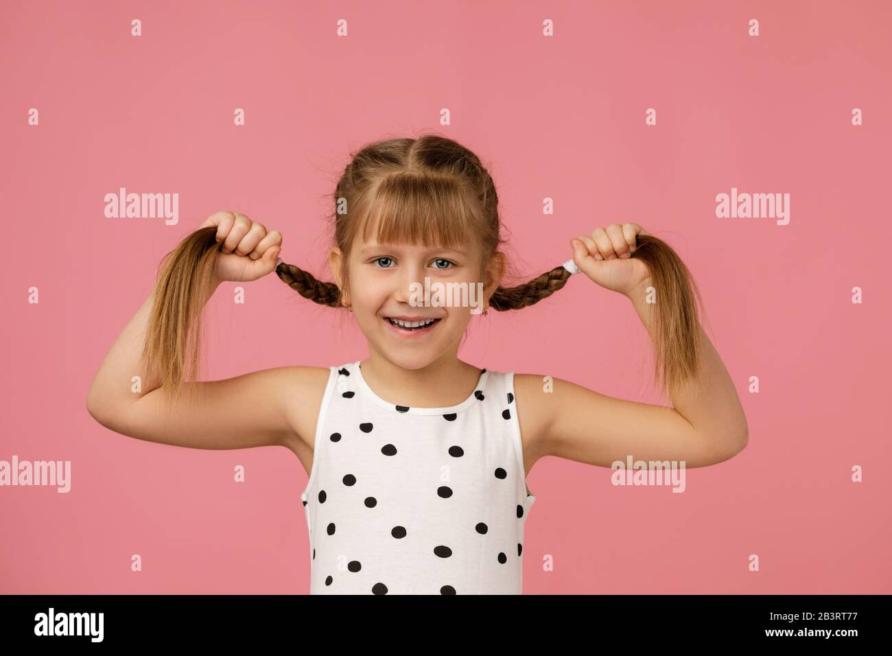 Süßes kleines Mädchen, das lange Haarflechten auf pinkfarbenem Hintergrund hält. Flechthaar. Stockfoto