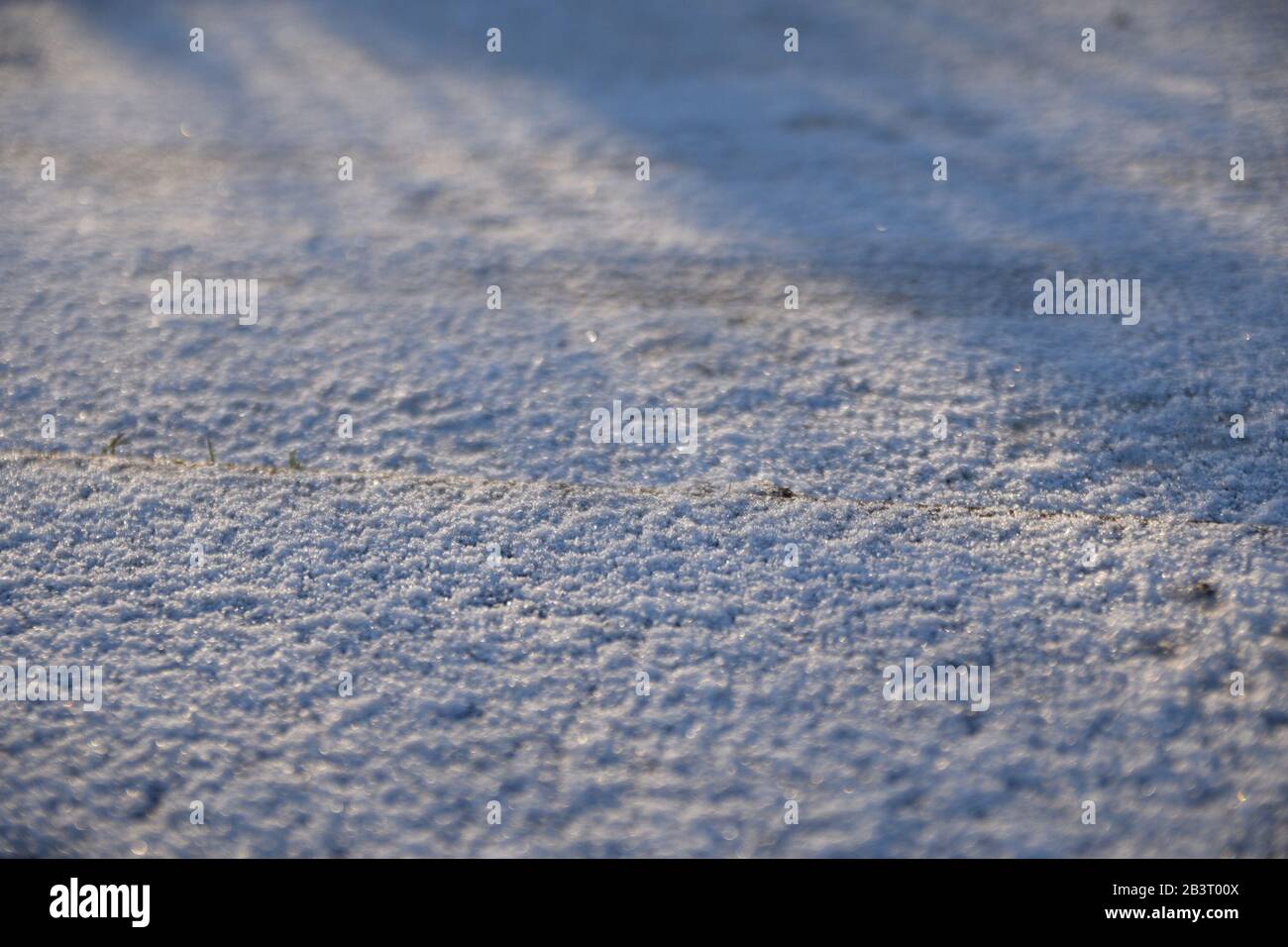 Erste Sonnenstrahlen werfen Schatten auf eine Schneedecke, um ihre Texturen zu zeigen. Ein großartiger Winter- oder Weihnachtshintergrund oder ein tolles Konzept. Stockfoto