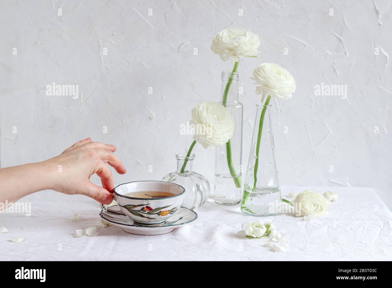 Tischeinstellung mit weißen Blumen und Frauenhand, die eine Tasse Tee hält Stockfoto