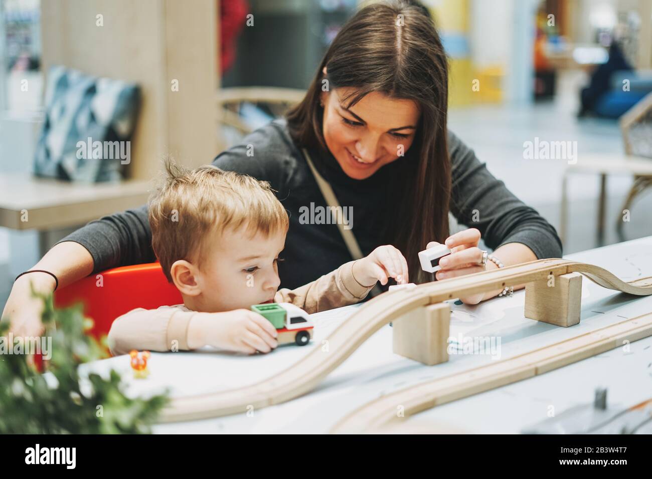 Süßes Kleinkind mit Mutter spielt mit Autotoys im Spielzimmer im Einkaufszentrum Stockfoto