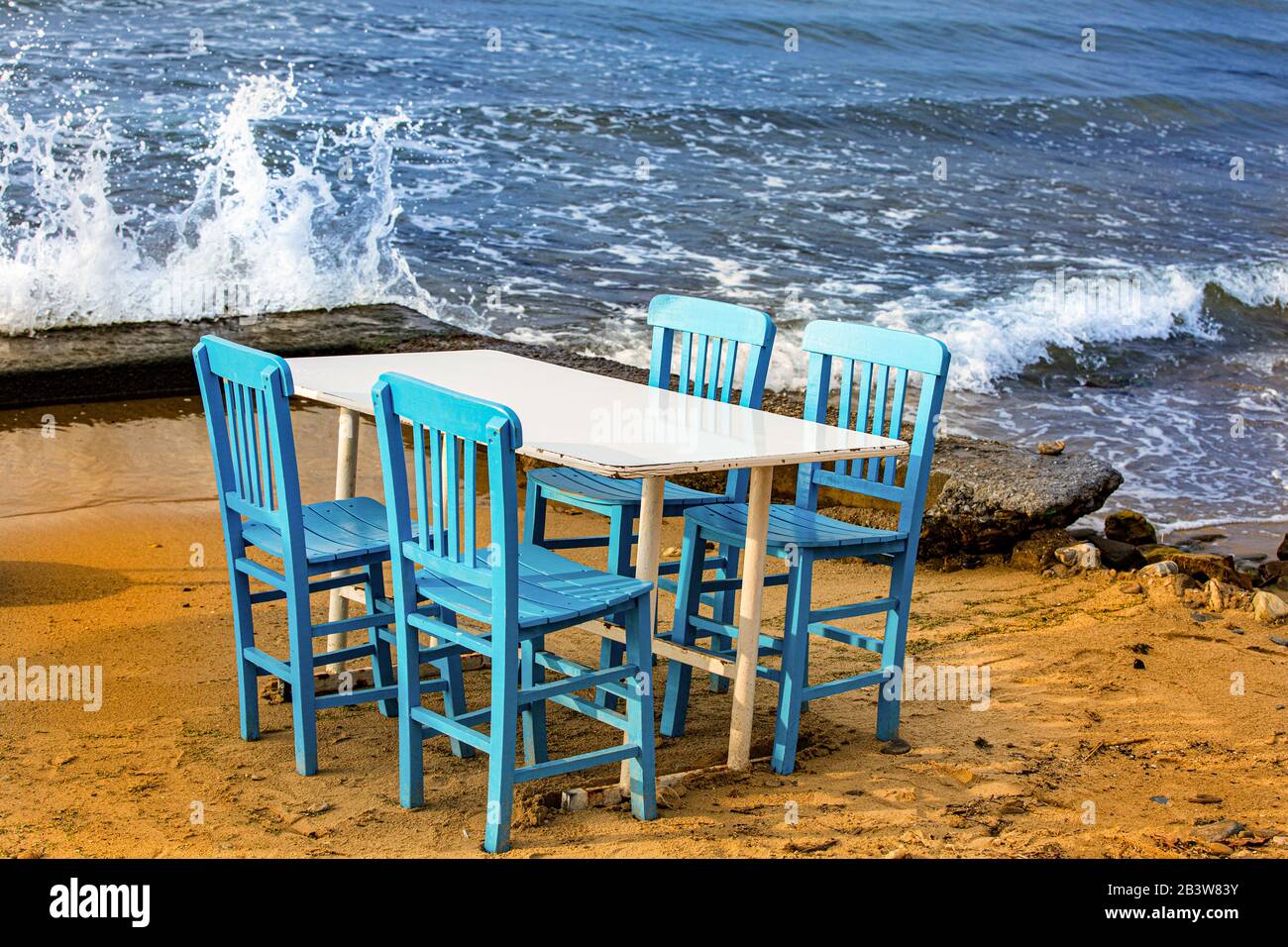 Tisch mit vier blauen Chaires am Strand. Wellen krachen auf das Ufer Stockfoto