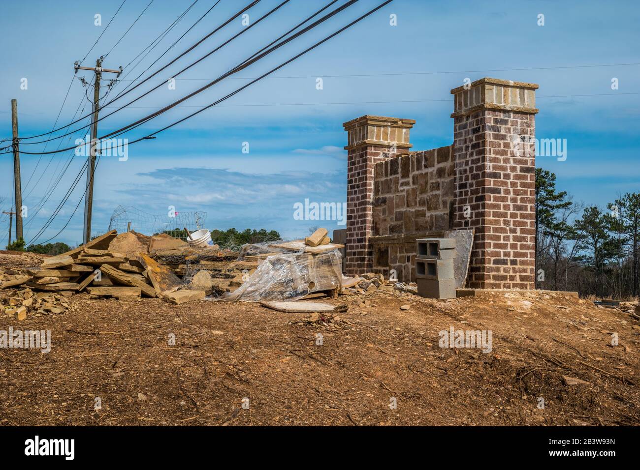 Baustelle einer neuen Gemeindemauer, die auf einem Hügel mit Backstein- und Steinblick mit Stromleitungen über dem Kopf an einem sonnigen Tag installiert wird Stockfoto