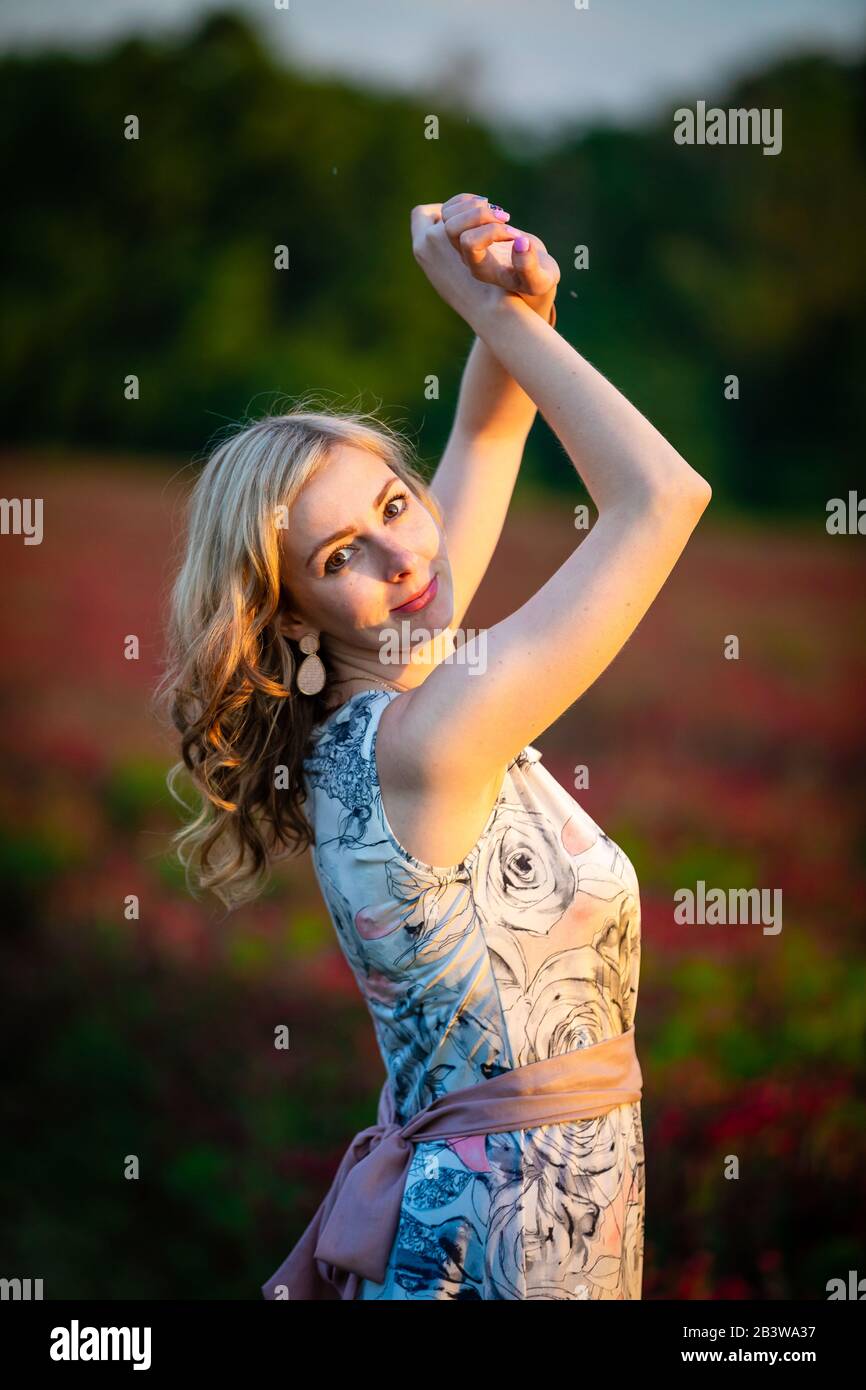 Junge Frau in rosafarbenem Kleid auf dem Feld des roten Kleeblatts in der Sonnenuntergangszeit Stockfoto