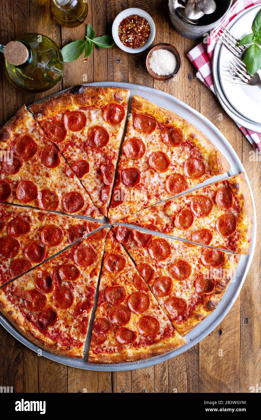 Große Pfefferoni Pizza auf Holztisch in rustikaler Umgebung Stockfoto